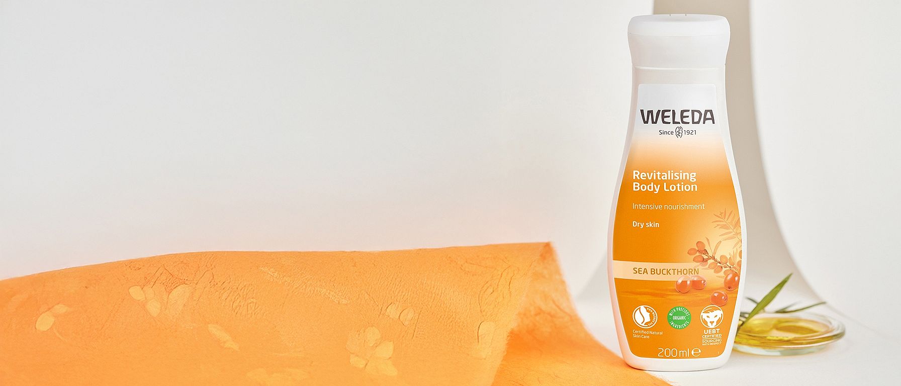 Revitalising Body Lotion - Sea Buckthorn on a grey baclground with orange fabric next to it.