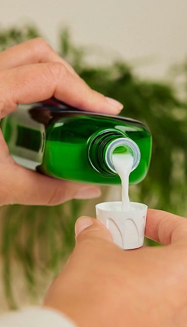 Weleda bath milk pouring from green bottle into bottle cap.