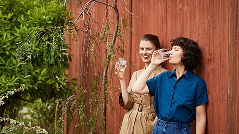 Women drinking water leaning on a wall.