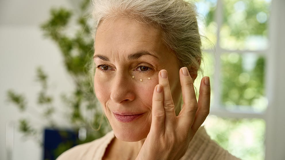 Mature woman dabbing eye cream on her face.